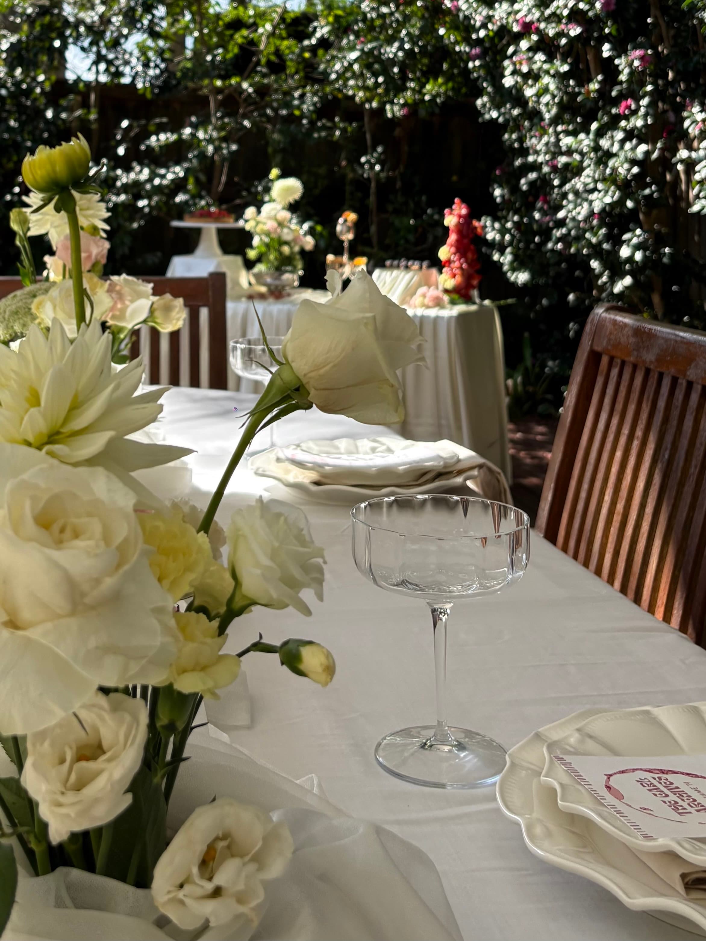 Styled outdoor reception table with florals, glassware, and layered place settings